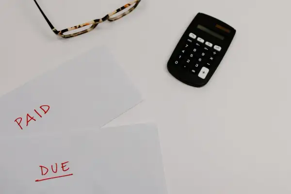 Okulary, kalkulator i kartki z napisami "PAID" i "DUE" na białym tle.