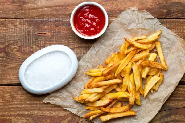 Domowe frytki na papierze, obok miseczka ketchupu i soli. Zastanawiasz się, ile kcal mają frytki domowe?
