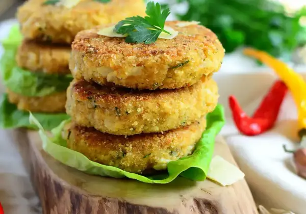 Złociste kotlety z kalafiora, chrupiące i aromatyczne, ułożone na sałacie. Obok czerwone i żółte papryczki chili.