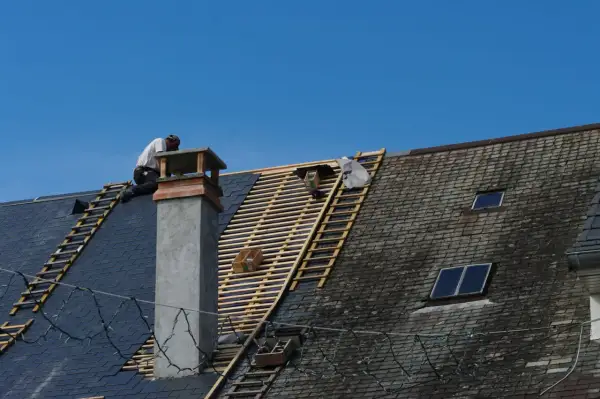 Un couvreur travaille sur un toit en ardoise, en cours de rénovation. Ces gros travaux pourraient ouvrir droit à une déduction fiscale pour le nu-propriétaire.