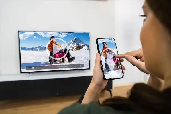 Oglądanie filmu z telefonu na TV przez WiFi. Dzieci zjeżdżają na sankach na ekranie telewizora i smartfona.