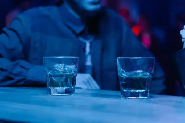 Dwa drinki na barze, a obok siedzi osoba. Czy można pić alkohol po radioterapii? To pytanie nurtuje wielu pacjentów.