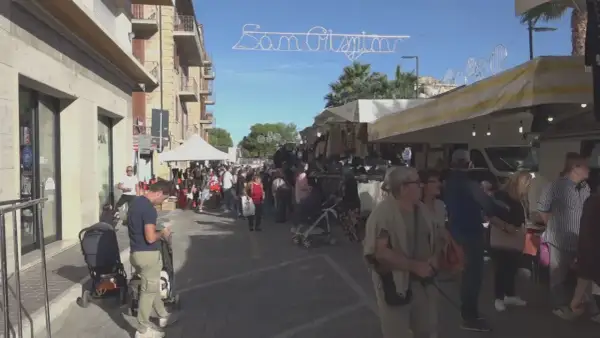 Festa San Crispino a Porto Sant'Elpidio: bancarelle affollate, gente che passeggia e acquista sotto un cielo azzurro.