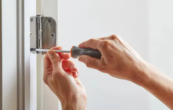 Mains serrant une vis avec un tournevis pour réparer une porte qui grince.