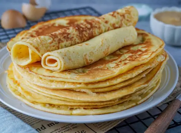 Ein Stapel goldbrauner Eierkuchen, zwei davon gerollt, warten auf ein leckeres Eierkuchen Rezept.