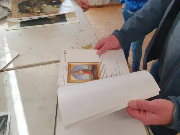 Hände halten ein Buch mit einem Bild eines Heiligen. Ein Detail der Kunstrestauration.