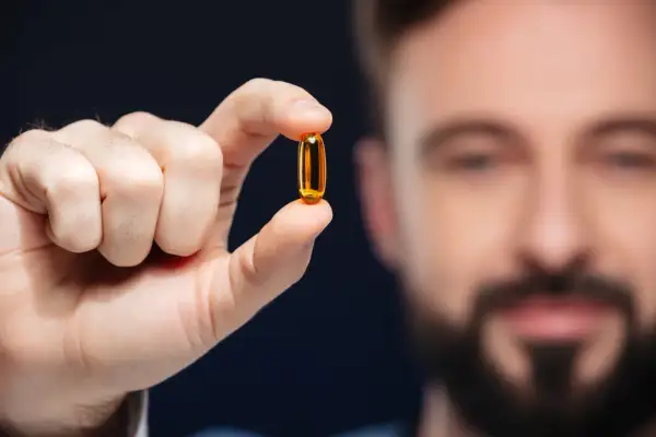 Mężczyzna trzyma kapsułkę z olejem rybim, bogatym w kwasy omega 3.