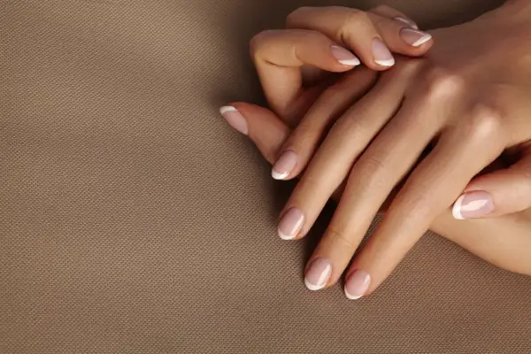 Dłonie z idealnym frenczem, podkreślającym naturalne kolory paznokci. Delikatny manicure na beżowym tle.