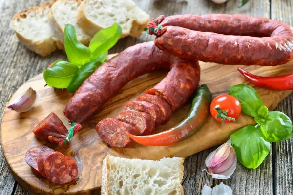 Chorizo co to? Pikantna kiełbasa, chleb, papryczki, pomidor i bazylia na desce.