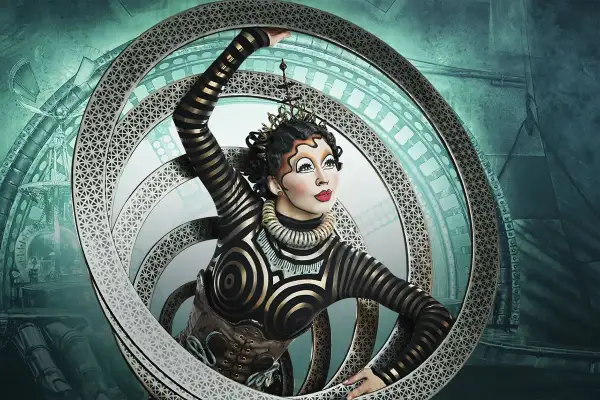 Artista del circo del sol en Zaragoza, con un traje de rayas doradas y negras, dentro de un aro metálico con intrincados diseños.