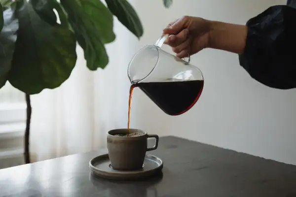 En hand häller upp mörkt kaffe ur en glaskanna i en mugg. Kaffet innehåller njutning och energi.