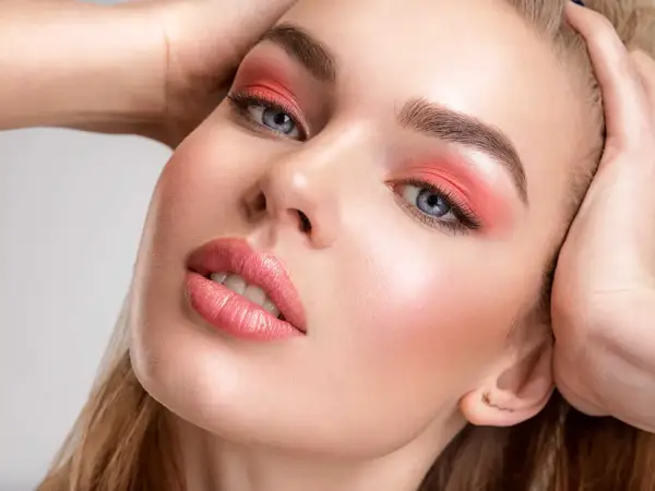 Viso di donna con ombretto corallo e un delicato blush o fard sulle guance.