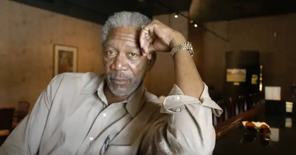 Morgan Freeman młody, z siwą brodą i zmarszczkami, opiera głowę na dłoni.