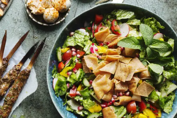 En fräsch fattoush-sallad med krispigt pitabröd, grönsaker och granatäppelkärnor. Bredvid ligger grillspett med kött.