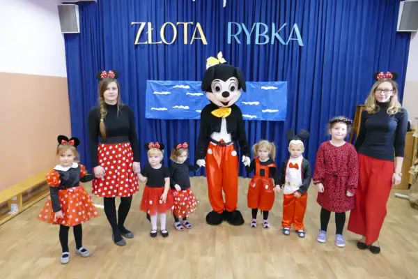 Dzieci i panie w strojach na dzień postaci z bajek, w tym Myszka Miki i Minnie, pozują do zdjęcia.