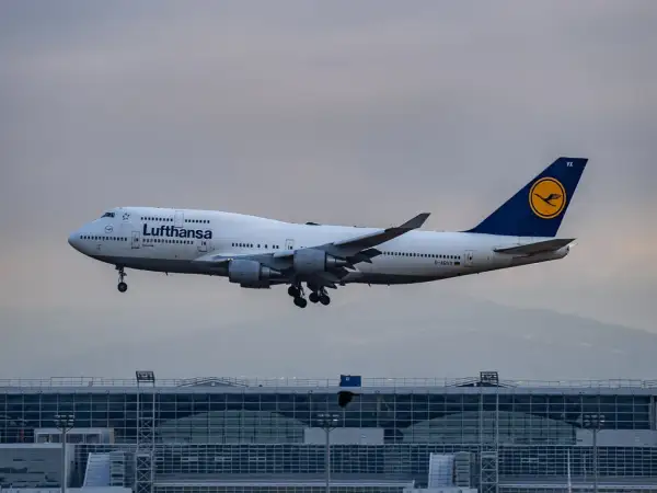 Lufthansa Boeing 747 im Landeanflug über einem modernen Flughafengebäude.
