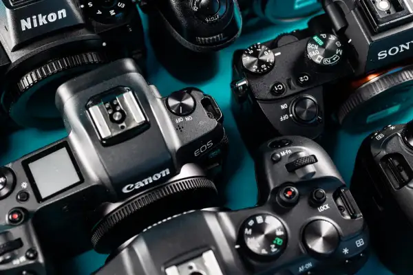 Zbliżenie na kilka aparatów fotograficznych marek Nikon, Canon i Sony, ułożonych na niebieskim tle.
