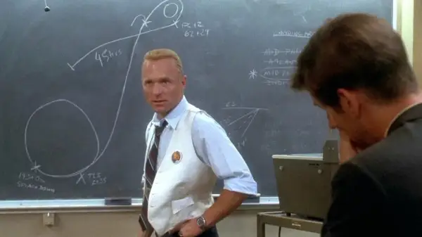 Gene Kranz, w białej kamizelce, omawia trajektorię misji Apollo 13 na tablicy.