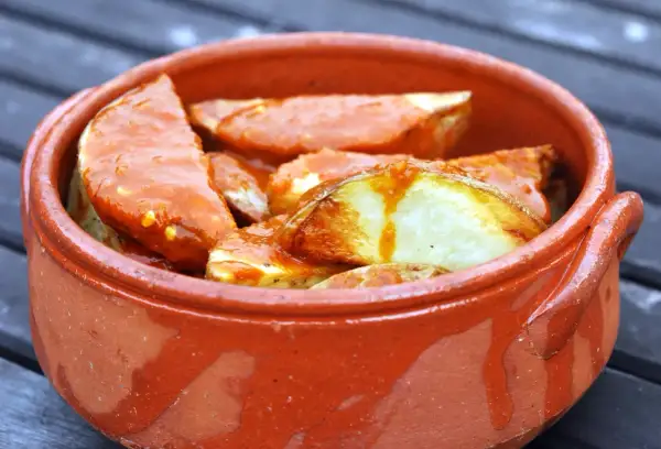 Patatas bravas, pommes de terre croustillantes nappées d'une sauce épicée, servies dans un plat en terre cuite.