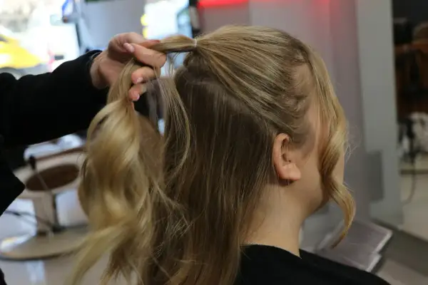 Tworzenie fryzury na Dzień Kobiet. Dłoń modeluje blond włosy, przygotowując je do stylizacji.