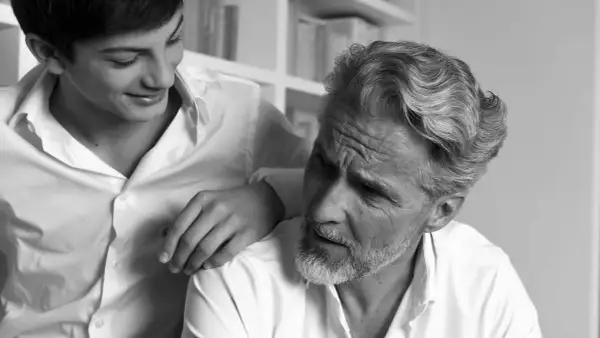 Un jeune homme pose sa main sur l'épaule d'un homme plus âgé, dont la barbe poil blanc est visible.