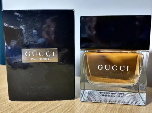 Elegancki zestaw z wodą po goleniu Gucci Pour Homme. Złocisty płyn w szklanym flakonie i czarne opakowanie.