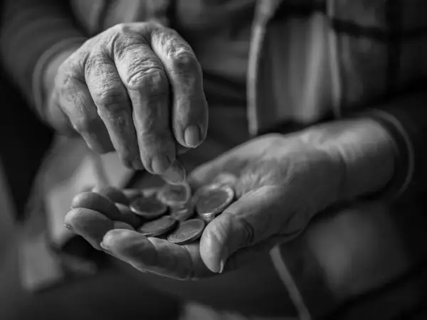 Mani anziane contano monete, un gesto che evoca la domanda su a quanto ammonta l'assegno di accompagnamento.