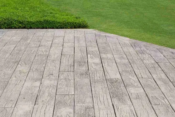 Pavimentazione marciapiede in cemento stampato effetto legno, adiacente a un prato verde ben curato.
