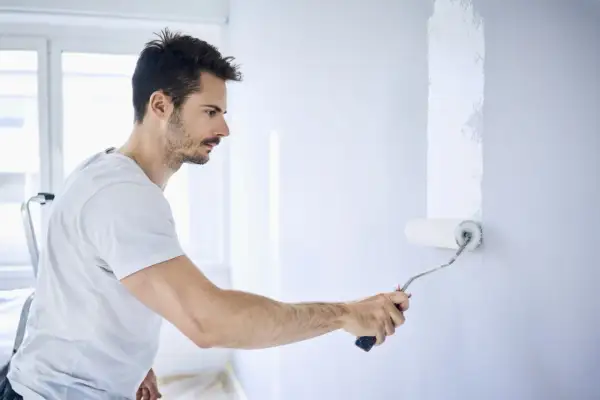 Mann streicht Wand mit weißer Farbe. Die Nachteile von Latexfarbe sind, dass sie schwer zu entfernen ist.