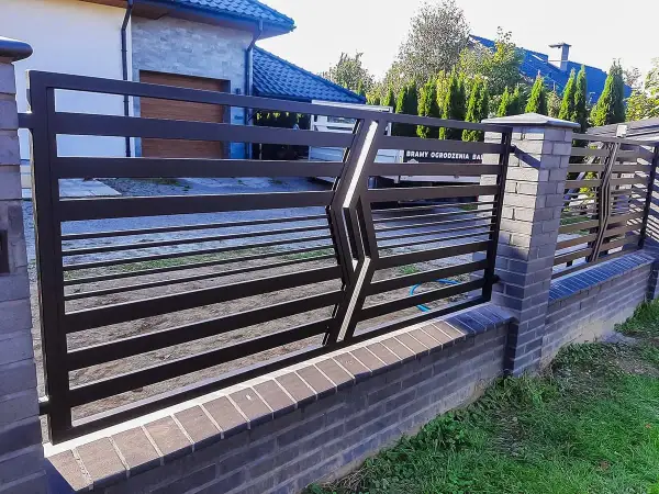 Nowoczesne, najładniejsze ogrodzenia kute z metalu, osadzone na ceglanym murku, tworzą elegancką barierę.
