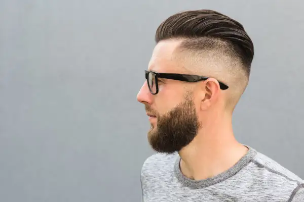 Mężczyzna z zarostem i modnym buzz cut, który sprytnie maskuje zakola.