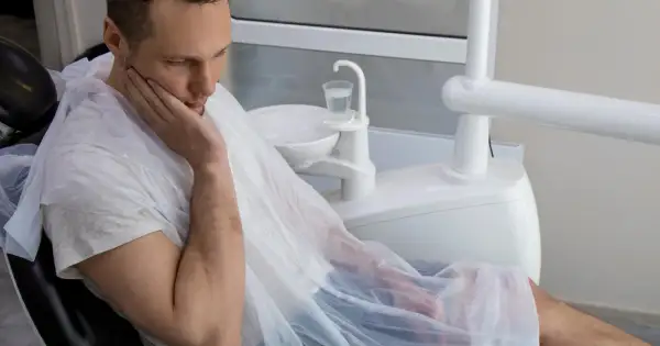 Mężczyzna w fotelu dentystycznym, z ręką na policzku, martwi się o swoje zdrowie. Czy to początek sepsy od zęba?