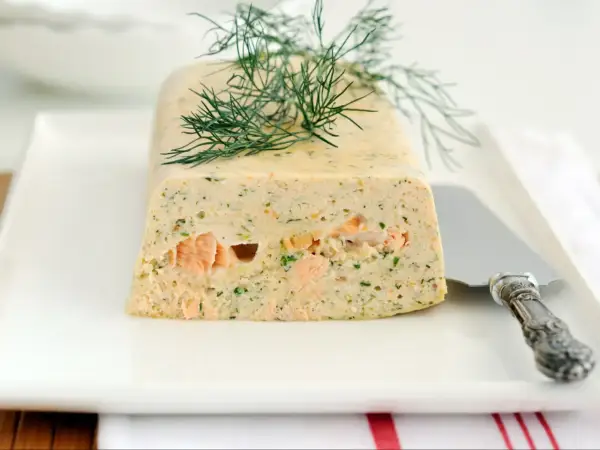 Elegancka terrina z łososia, ozdobiona gałązką koperku, prezentuje się apetycznie na białym talerzu.