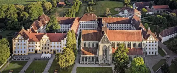 Luftaufnahme eines beeindruckenden schloss im Bodenseekreis mit roten Ziegeldächern, umgeben von grünen Bäumen und gepflegten Gärten.
