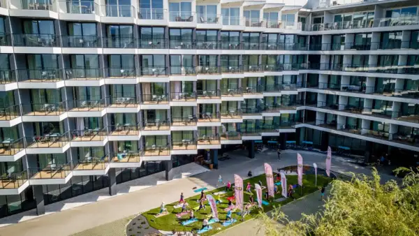Grupa osób ćwiczy jogę na trawniku przed nowoczesnym seaside park hotel.
