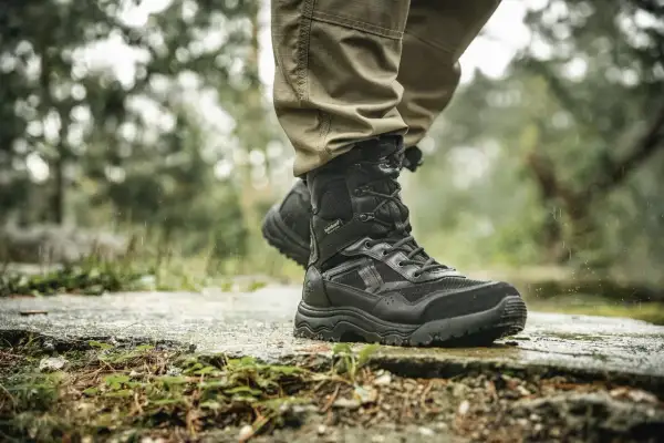 Czarne buty trekkingowe na mokrej kamiennej ścieżce w lesie.
