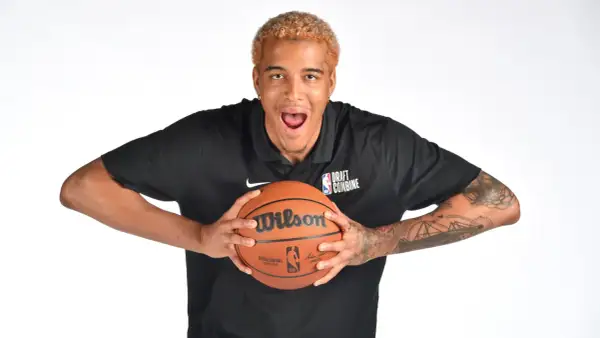 Młody polak w NBA, z blond włosami i tatuażami na ramionach, trzyma piłkę do koszykówki.