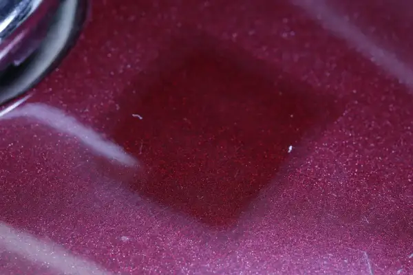 Superficie metallizzata color bordeaux con riflessi scintillanti. Il trasparente è un colore che cattura la luce, creando un effetto quasi liquido.