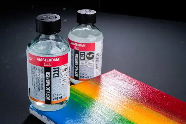 Due flaconi di vernice acrilica Amsterdam, uno lucido e uno opaco, accanto a una tavolozza arcobaleno. Ricorda che la vernice acrilica è tossica.