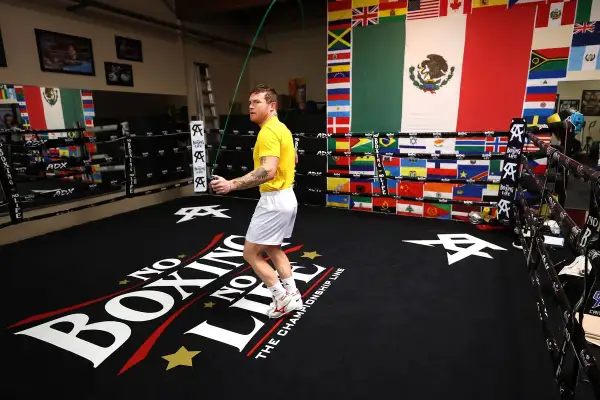Boxer in yellow shirt doing a boxing jump rope workout in a ring decorated with flags.