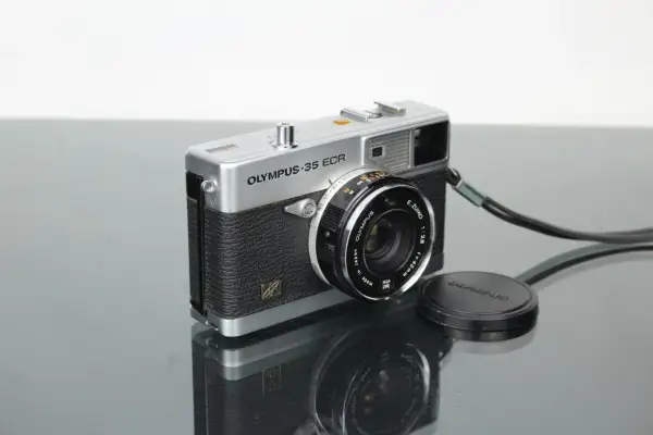 A vintage silver Olympus 35 ECR rangefinder camera with a black textured grip sits on a reflective surface.