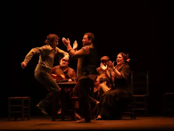 Artistas de flamenco, con guitarras y palmas, dan vida a la escena. El significado de "jalear" se siente en la energía.