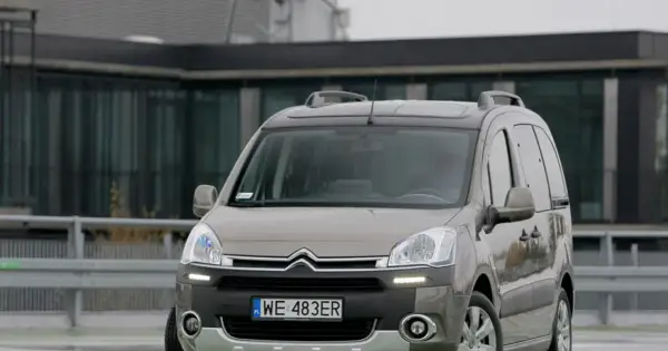 Szary Citroen Berlingo 1.6 HDI z relingami dachowymi zaparkowany przed nowoczesnym budynkiem.