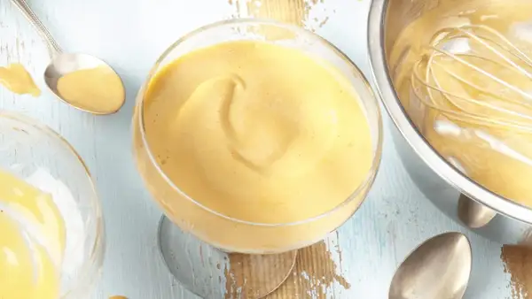 Cremiges Zabaione-Rezept in einem Glas, Löffel daneben. Ein Schneebesen ruht in einer Schüssel mit der köstlichen Masse.