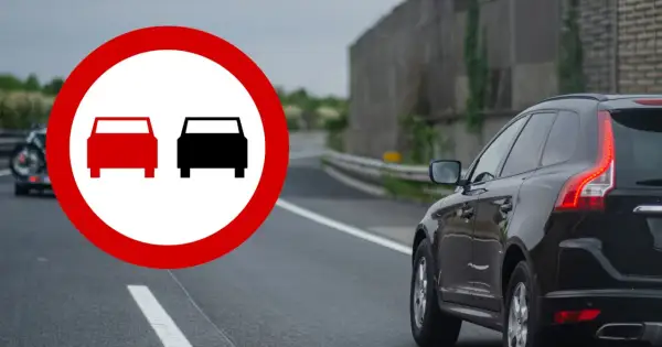 Znak zakazu wyprzedzania na drodze jednokierunkowej. Czarny SUV jedzie po drodze, gdzie wyprzedzanie jest zabronione.