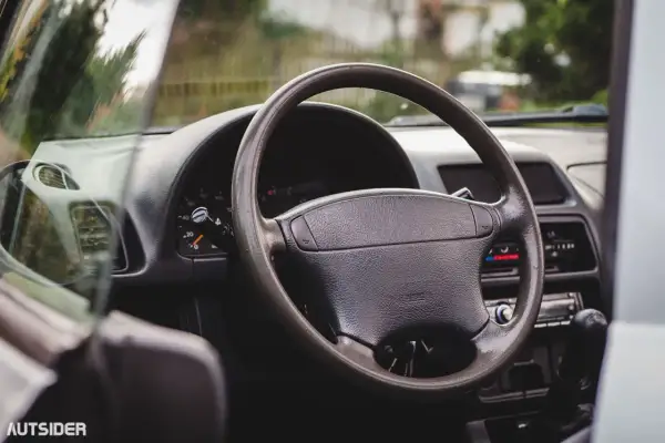 Wnętrze Suzuki X90: kierownica, deska rozdzielcza z zegarami i radiem, widok z perspektywy kierowcy.