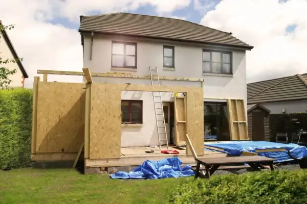 Ein **Anbau Haus** im Bau. Holzkonstruktion und OSB-Platten bilden die Wände des neuen Gebäudeteils. Blaue Planen schützen Baumaterialien.