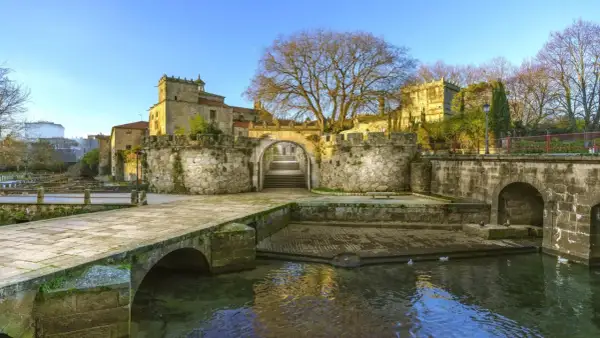 El pazo Vista Alegre, con su puente de piedra y río, se alza majestuoso bajo un cielo azul.
