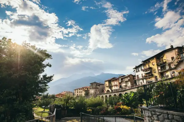 Case colorate si affacciano su un fiume, incorniciate da montagne e cielo azzurro. Un incantevole scorcio dei borghi di Brescia.