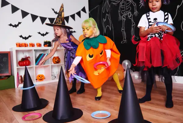Niñas disfrazadas de bruja y calabaza juegan a lanzar aros en sombreros de bruja, parte de divertidos juegos de Halloween para niños.